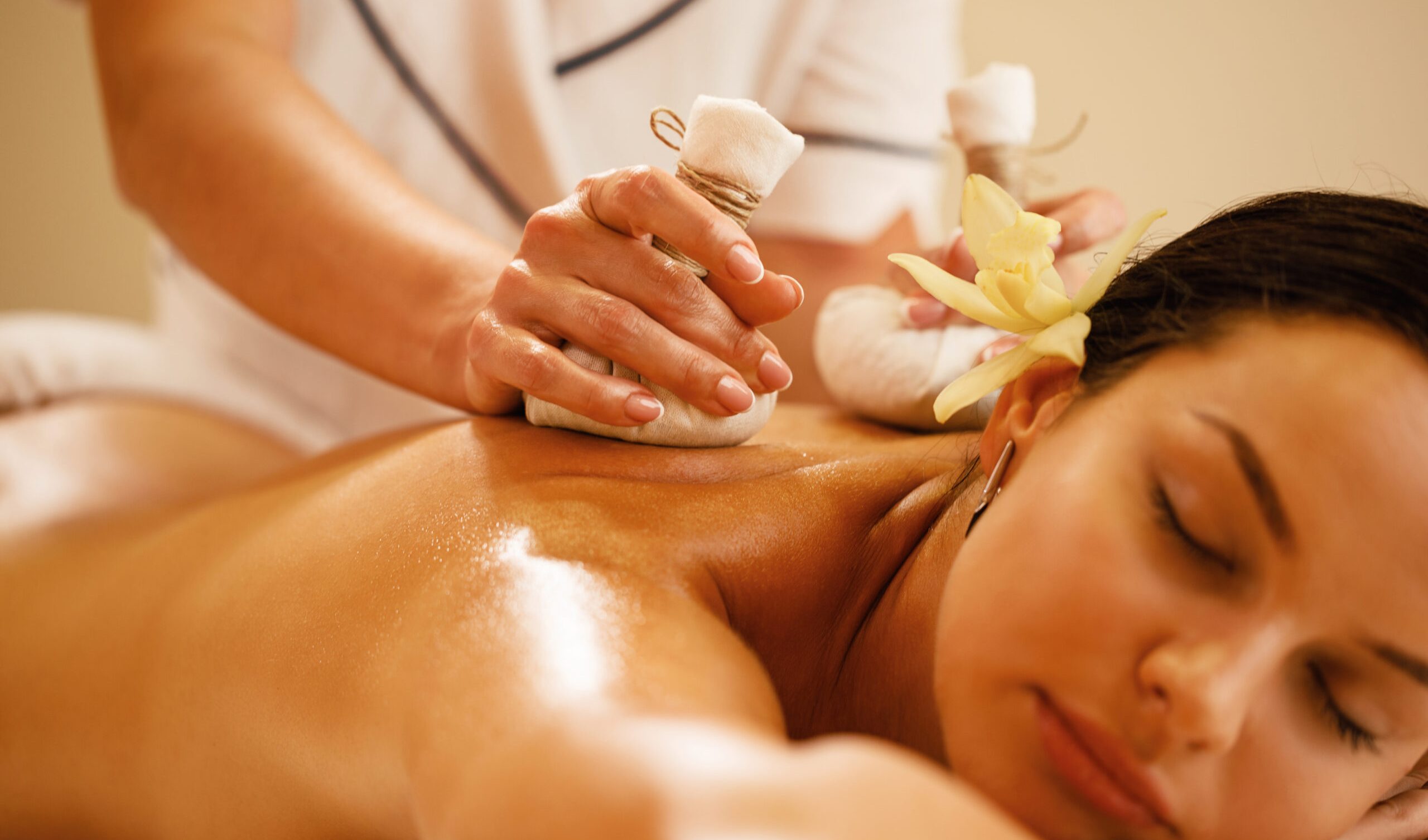 Close-up of relaxed woman getting back massage with herbal balls at health spa.